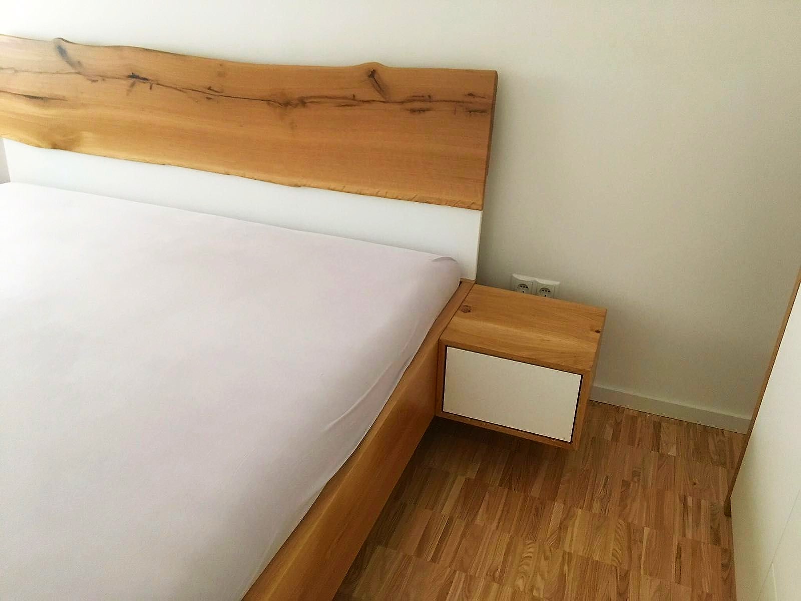 Eichenbett mit markantem Baumkanten-Kopfteil und daneben ein schwebender Nachttisch.