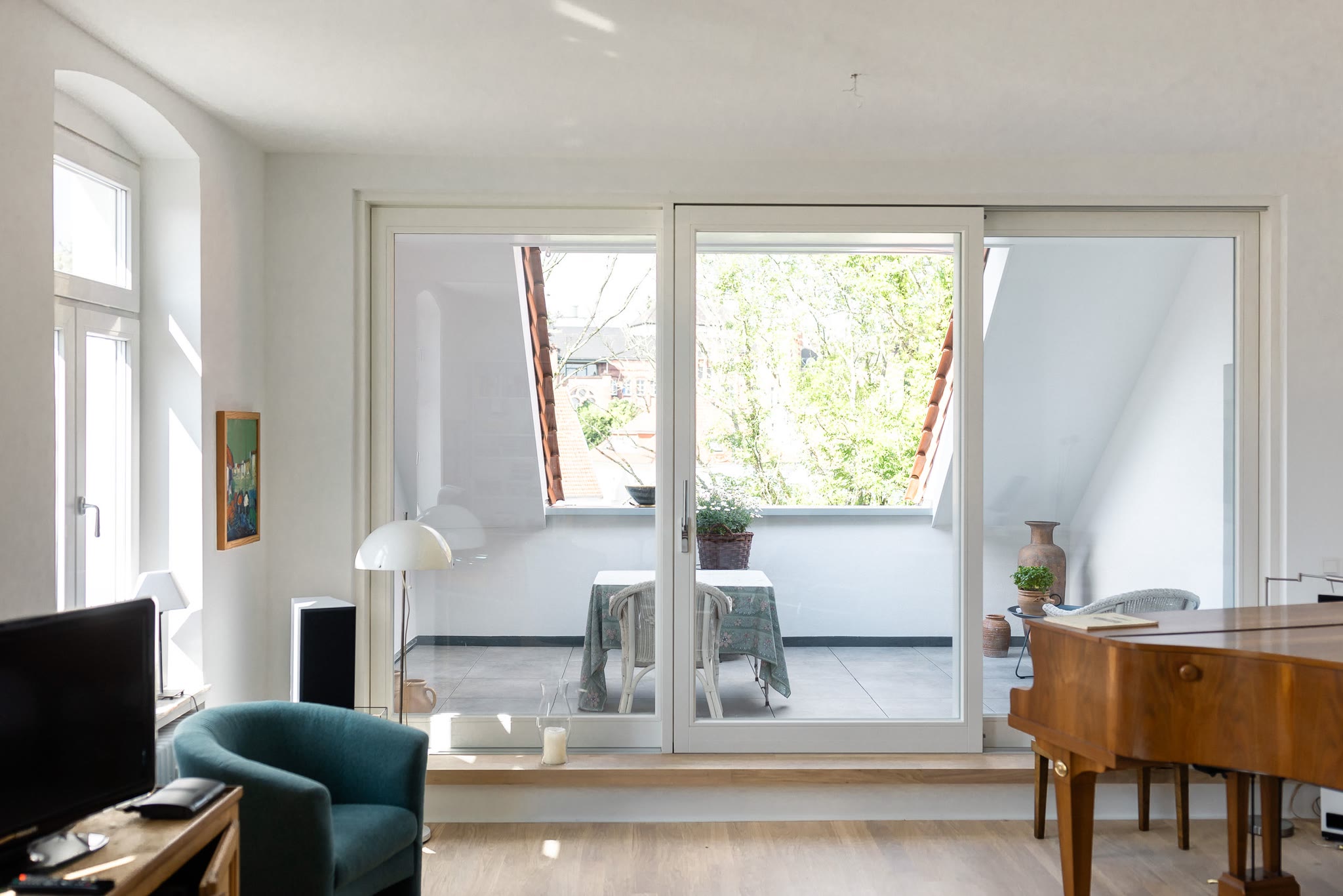 Helles Wohnzimmer mit großer weißer Hebe-Schiebetür zur Dachterrasse, davor Sessel und Flügel