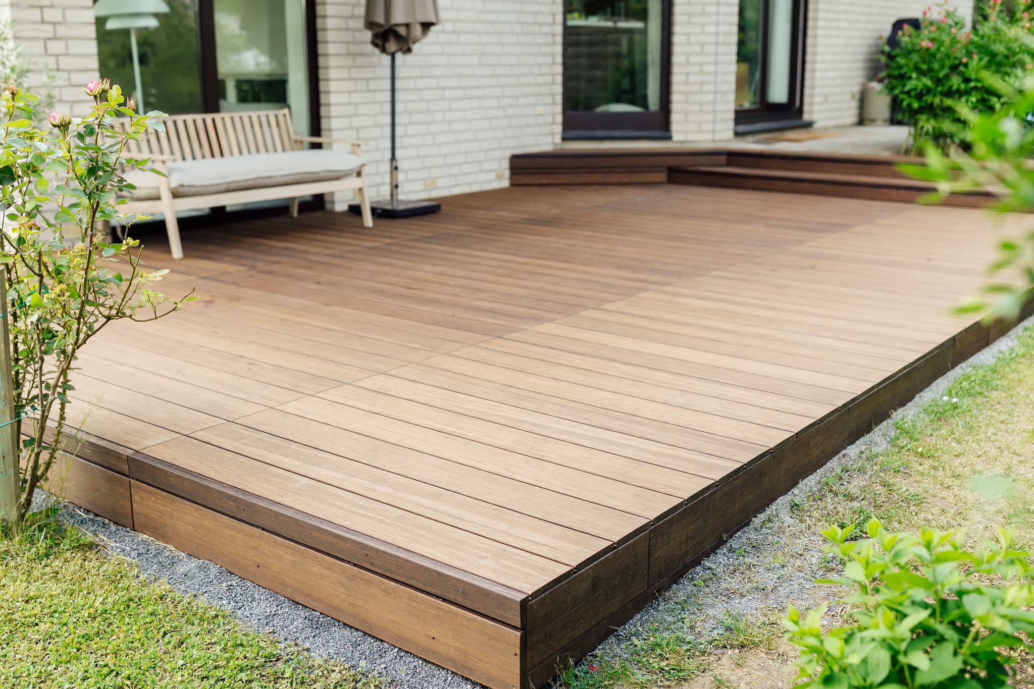 Fertige Terrasse aus dunklen Bambusdielen entlang einer weißen Klinkerfassade mit Stufe und Randblende